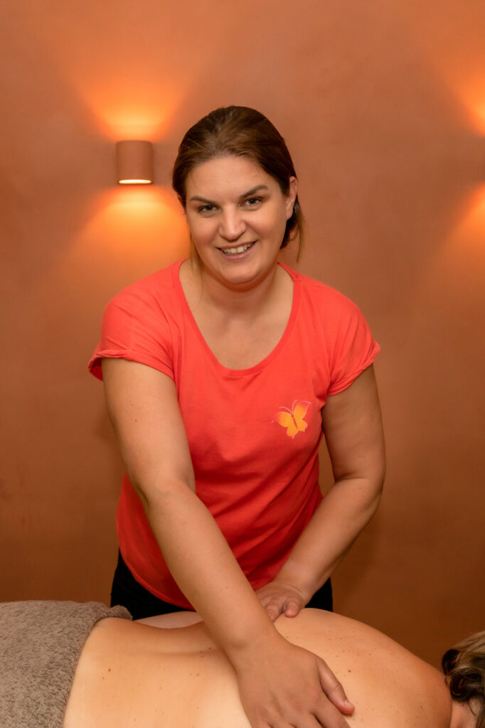 Els geeft lachend een rugmassage aan een klant in de sfeervolle behandelruimte
